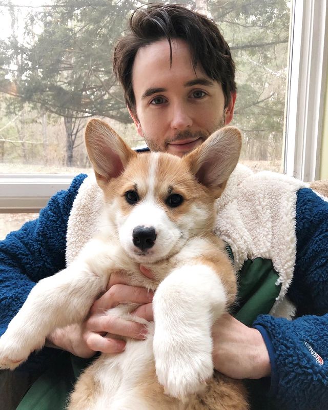 Garett Hawe in a blue sweater holding his pet dog.